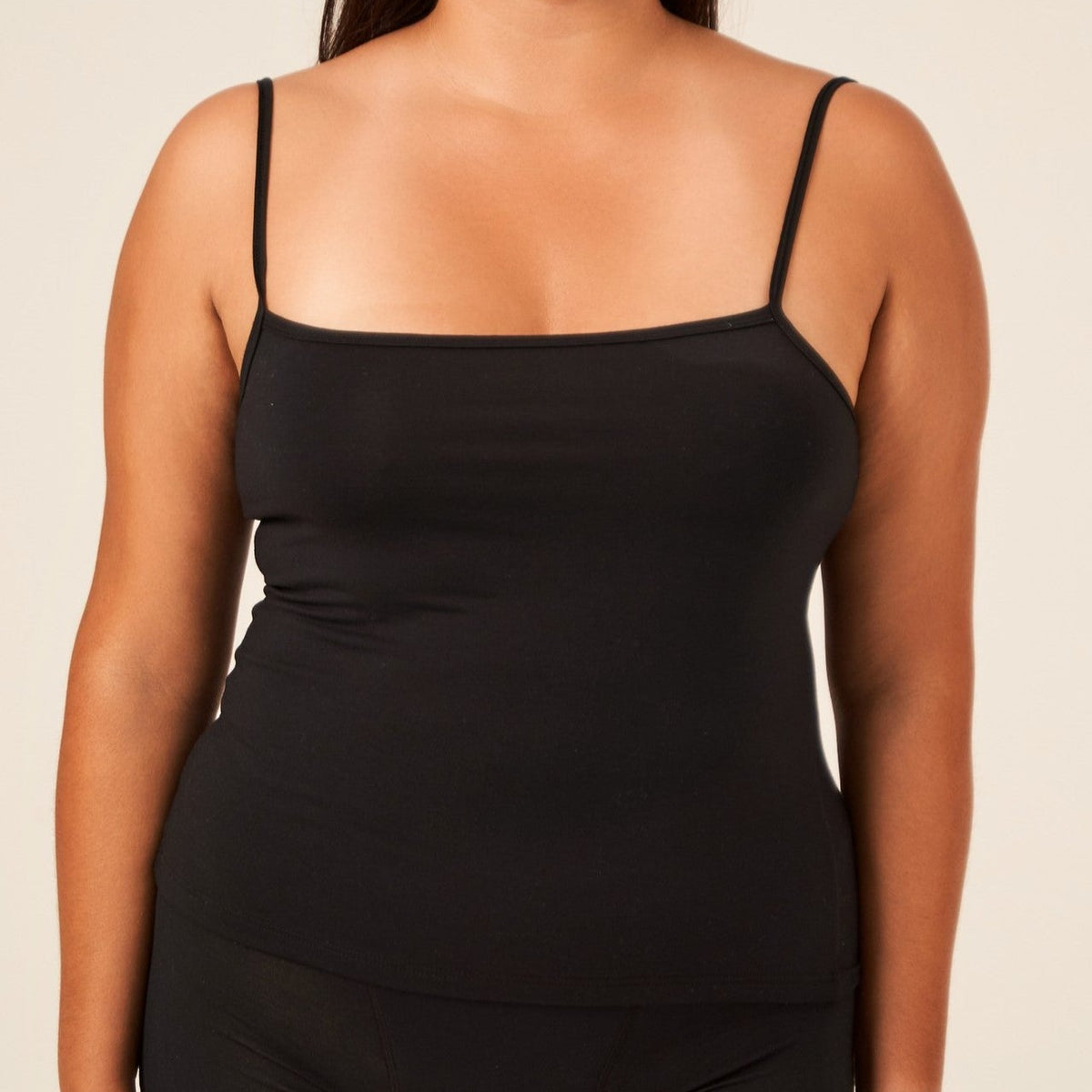 A woman wearing a black TENCEL™ camisole with adjustable straps and matching briefs