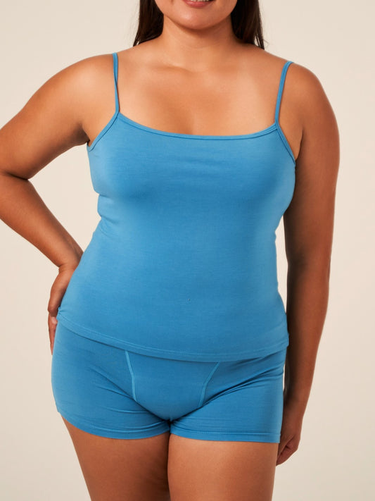 A woman wearing a blue TENCEL™ camisole with adjustable straps and matching briefs