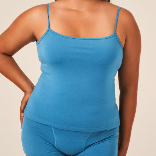 A woman wearing a blue TENCEL™ camisole with adjustable straps and matching briefs
