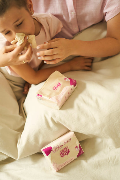 Child and mother in bed blowing nose with Gentle Day lotion tissue